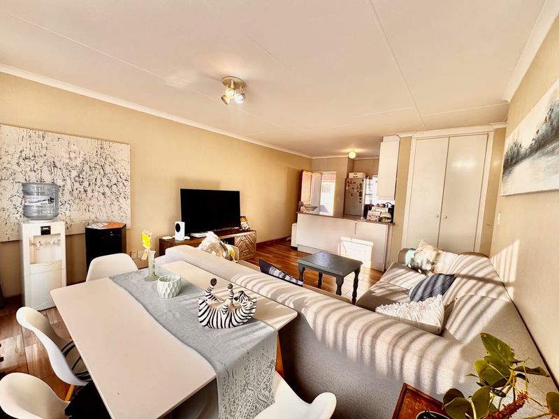 An open-plan living and dining area featuring hardwood flooring, a breakfast bar, and built-in storage cupboards, creating a functional and connected living space.
