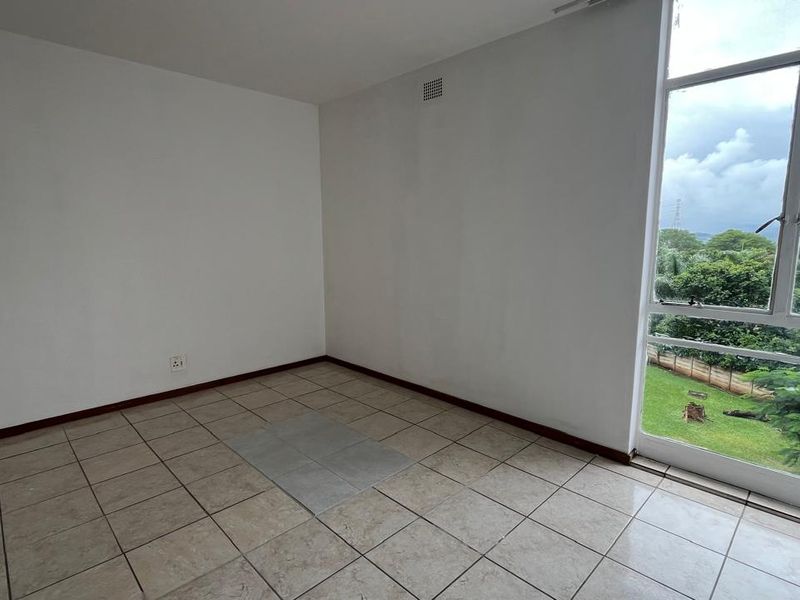 An empty bedroom featuring tiled flooring, a large window with exterior views, and a neutral wall finish, ready for personalization.