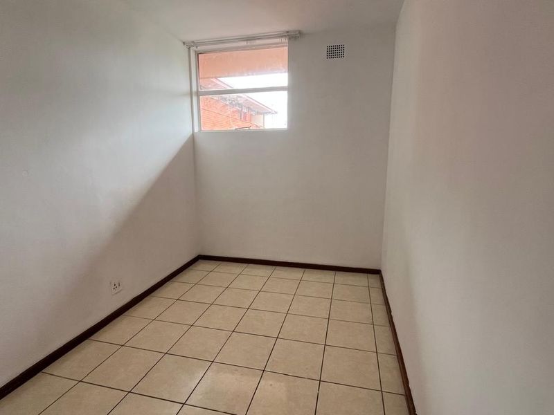 A compact, empty bedroom featuring neutral tiled flooring and a single window, providing a blank canvas for potential interior design and furnishing.