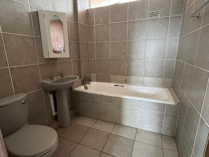 A dated bathroom featuring a pedestal basin, bathtub, and toilet with full-height wall tiling and floor tiles, requiring cosmetic updates.