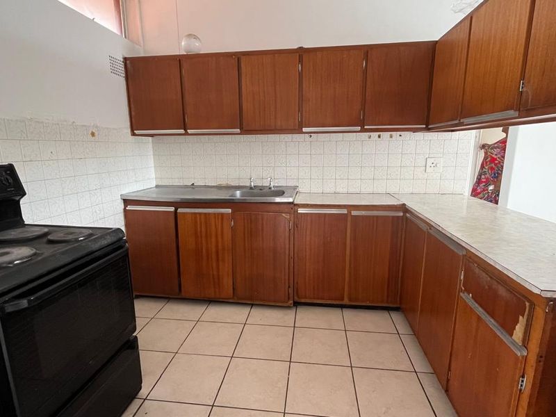 A dated kitchen featuring original wooden cabinetry, laminate countertops, tiled backsplash, and tiled flooring, offering significant potential for modernization and renovation.
