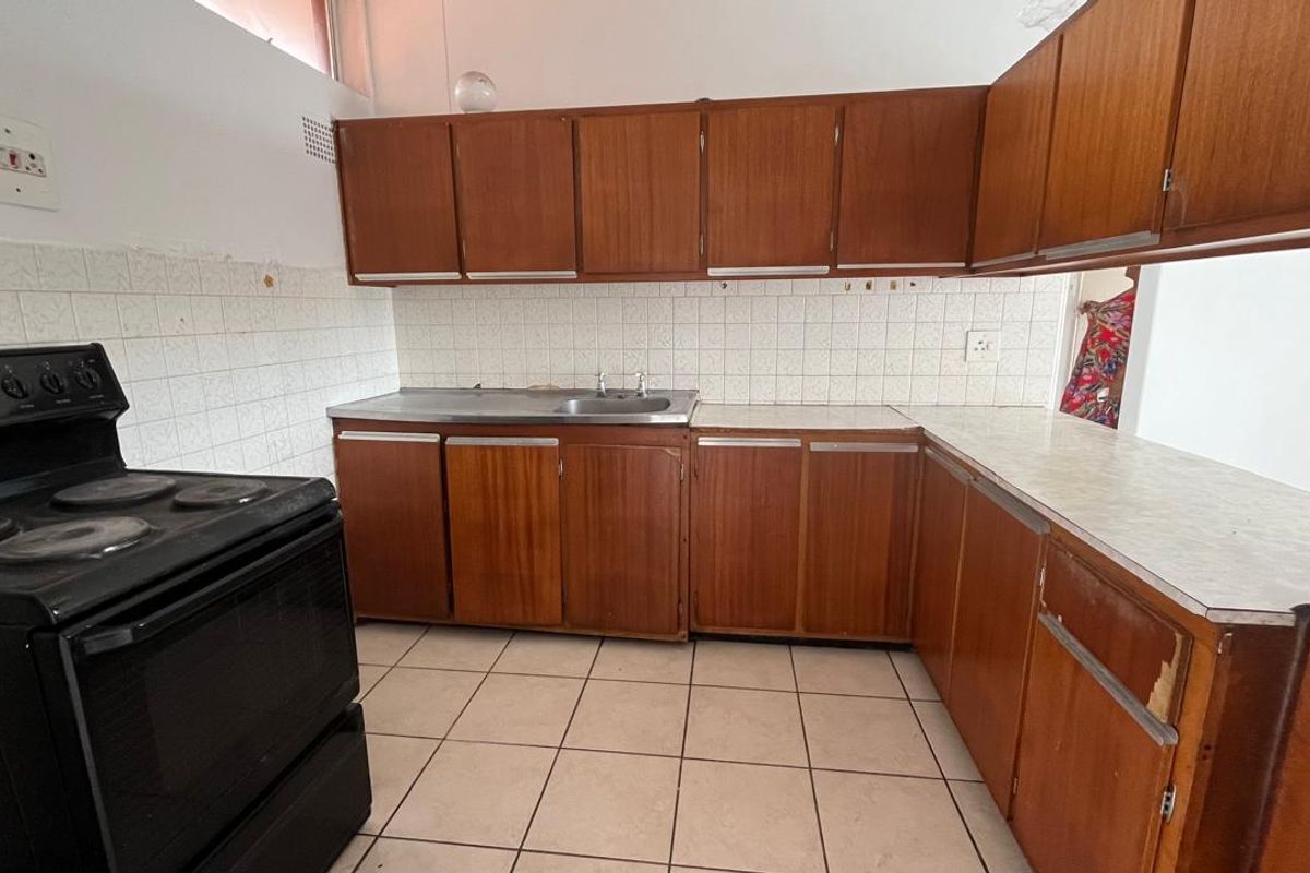 A dated kitchen featuring original wooden cabinetry, laminate countertops, tiled backsplash, and tiled flooring, offering significant potential for modernization and renovation.