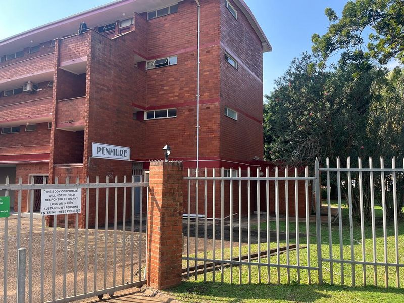 Exterior view of the Penmure apartment complex featuring a face brick facade, secure metal perimeter fencing, and established garden surroundings.