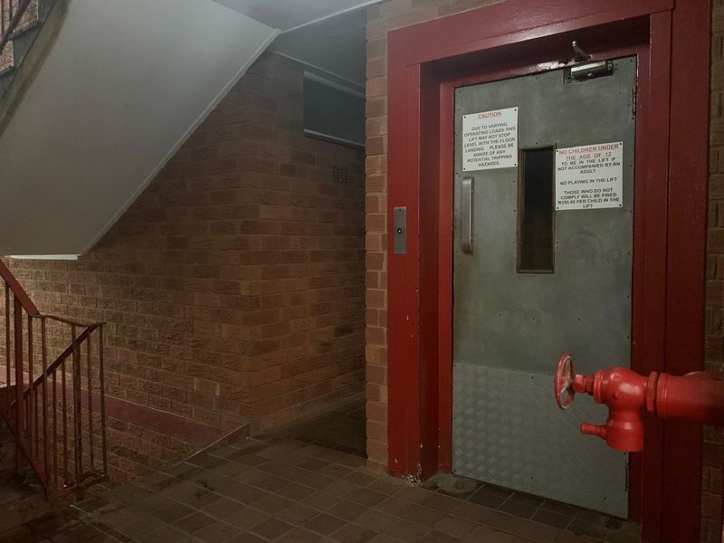 A communal apartment building landing featuring a lift entrance, staircase, and fire hydrant equipment.