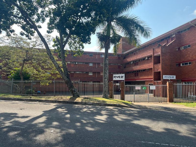 Street view of the Penmure apartment complex, featuring a multi-story brick facade, secure gated entrance, and perimeter fencing.