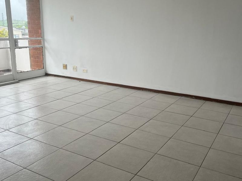 An empty living room featuring neutral tiled flooring, white walls, and a sliding glass door providing access to an outdoor area.