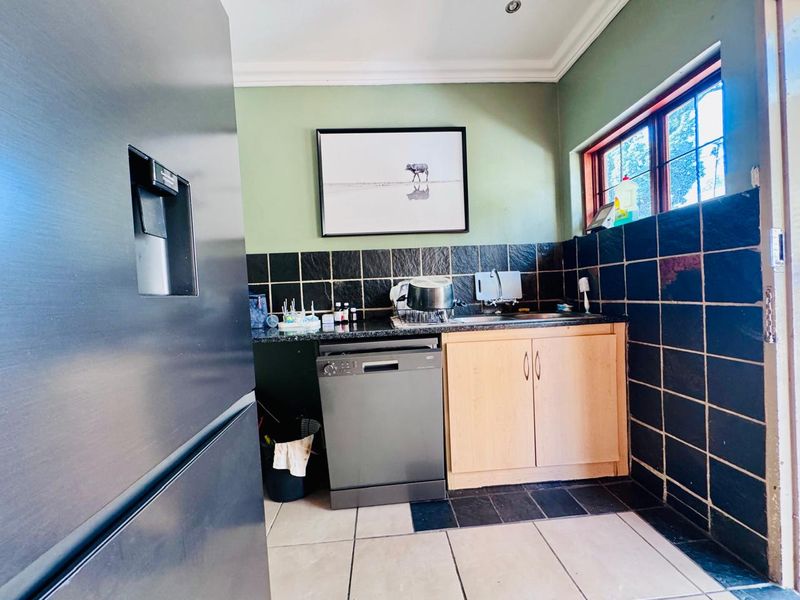 A functional scullery area featuring dark tiled splashbacks, light wood cabinetry, a stainless steel sink, and space for a dishwasher.