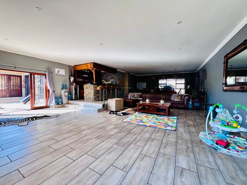 Spacious open-plan living area featuring wood-look tile flooring, recessed downlighting, and a built-in bar with stone cladding, leading out to a patio.