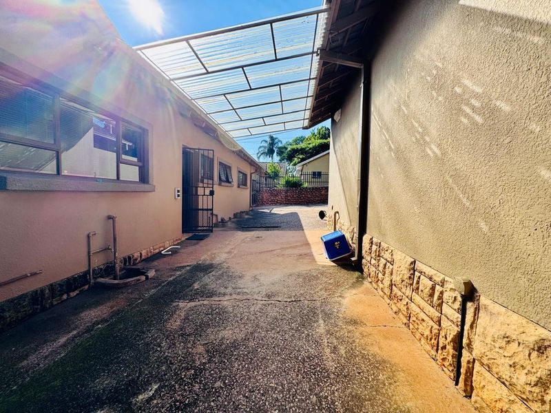 A narrow exterior side passage featuring a translucent corrugated roof covering, concrete flooring, and stone-clad wall accents.