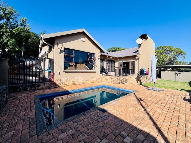 Rear view of the house featuring a paved pool area, brick cladding, and a raised patio with metal railings.