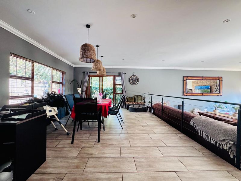 An open-plan living and dining area featuring tiled flooring, recessed ceiling lighting, and large windows providing natural light and access to the outdoors.