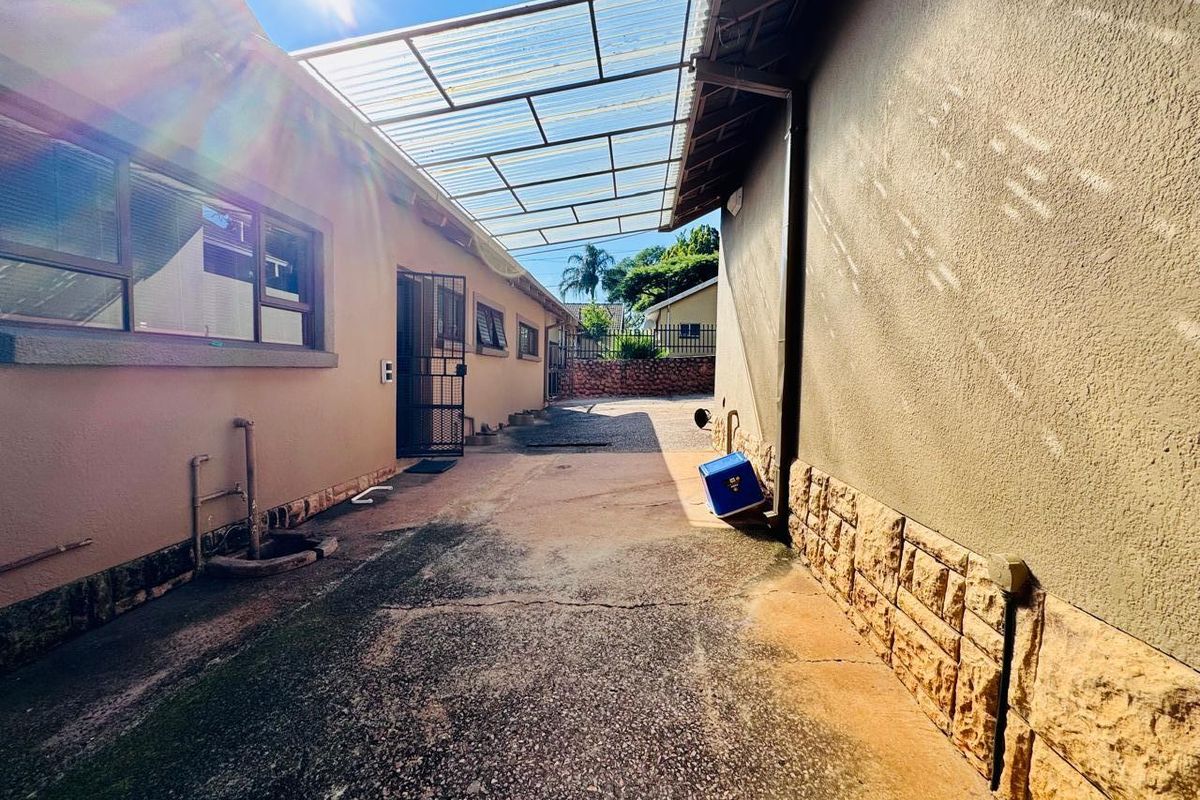 A narrow exterior side passage featuring a translucent corrugated roof covering, concrete flooring, and stone-clad wall accents.