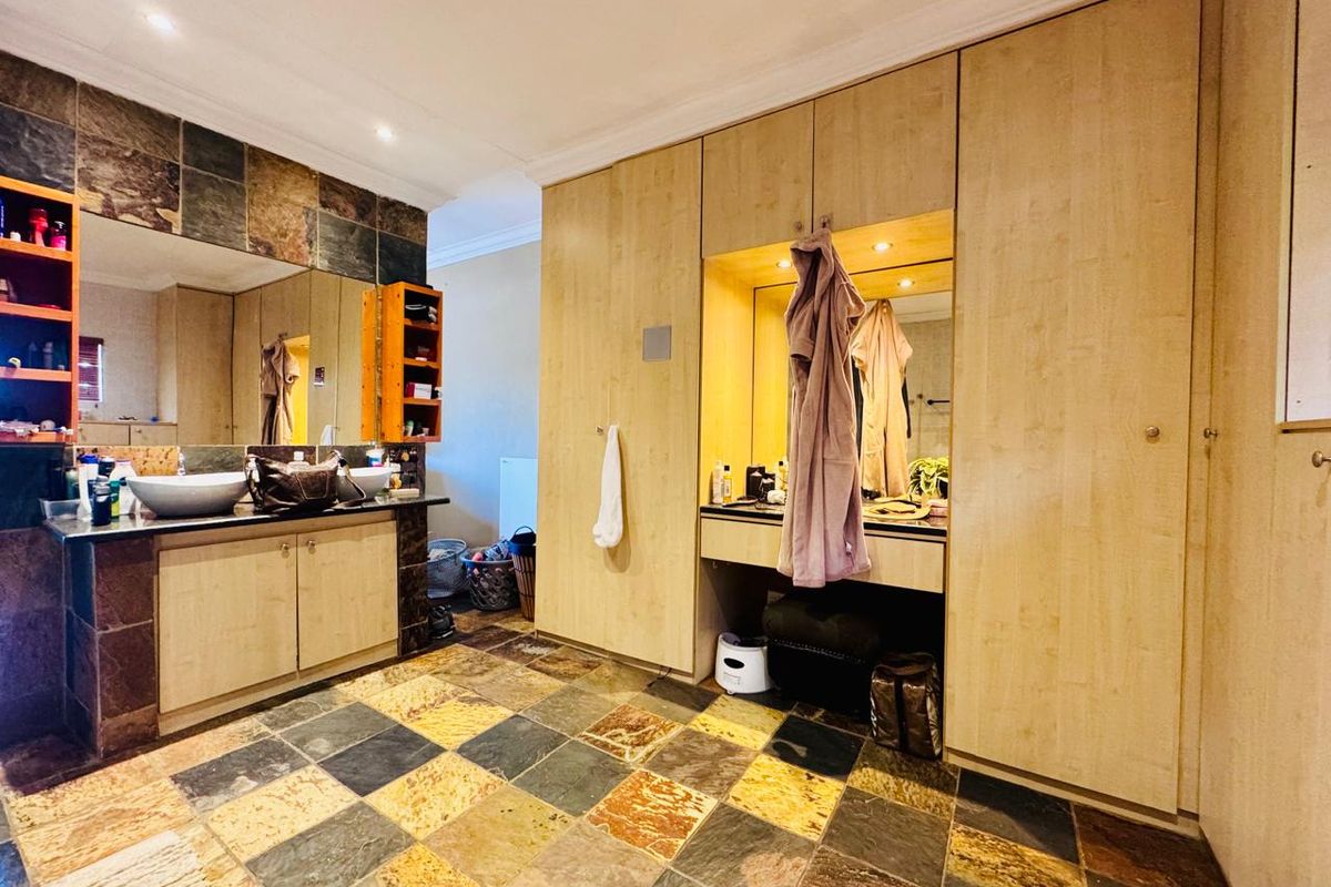 Spacious bathroom featuring dual vessel sinks, extensive built-in cabinetry, a dedicated vanity area, and natural stone floor tiling.