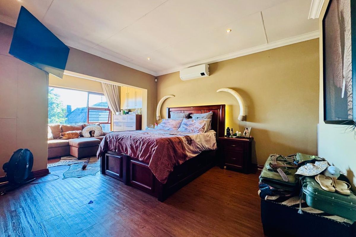 Spacious bedroom featuring wood-look flooring, recessed ceiling lighting, and a wall-mounted air conditioning unit, with an integrated seating area by the window.