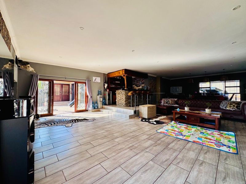 Spacious open-plan living area featuring a built-in stone-clad bar, tiled flooring, and large sliding doors providing seamless access to the outdoor patio.