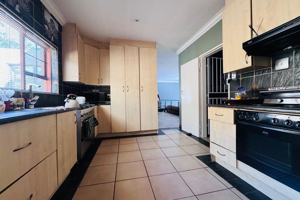 Functional kitchen featuring light wood-toned cabinetry, dark tiled splashbacks, tiled flooring, and a built-in oven with extractor fan.