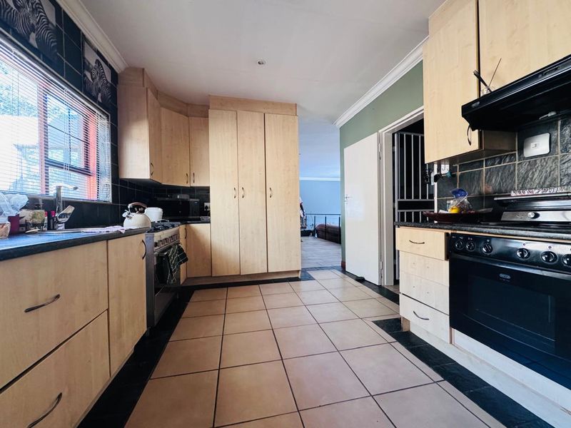 Functional kitchen featuring light wood-toned cabinetry, dark tiled splashbacks, tiled flooring, and a built-in oven with extractor fan.