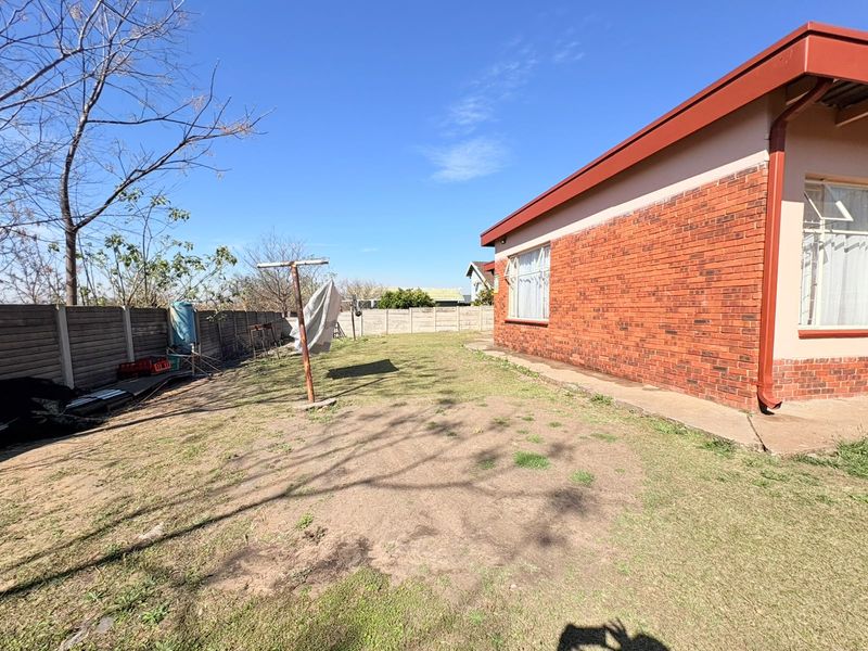 A spacious rear garden featuring a face brick exterior, concrete boundary walls, and a functional washing line area with potential for landscaping.