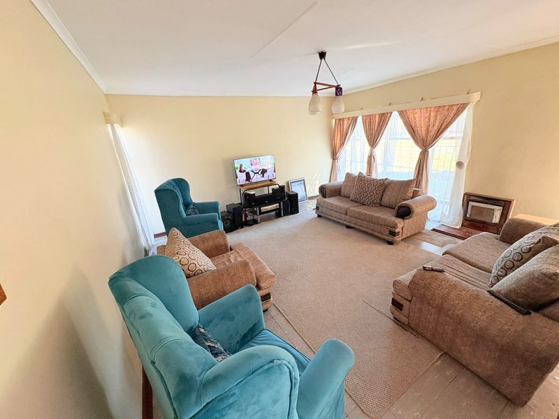 A spacious living room featuring tiled flooring, large windows with natural light, and classic cove cornicing, offering a comfortable area for relaxation.