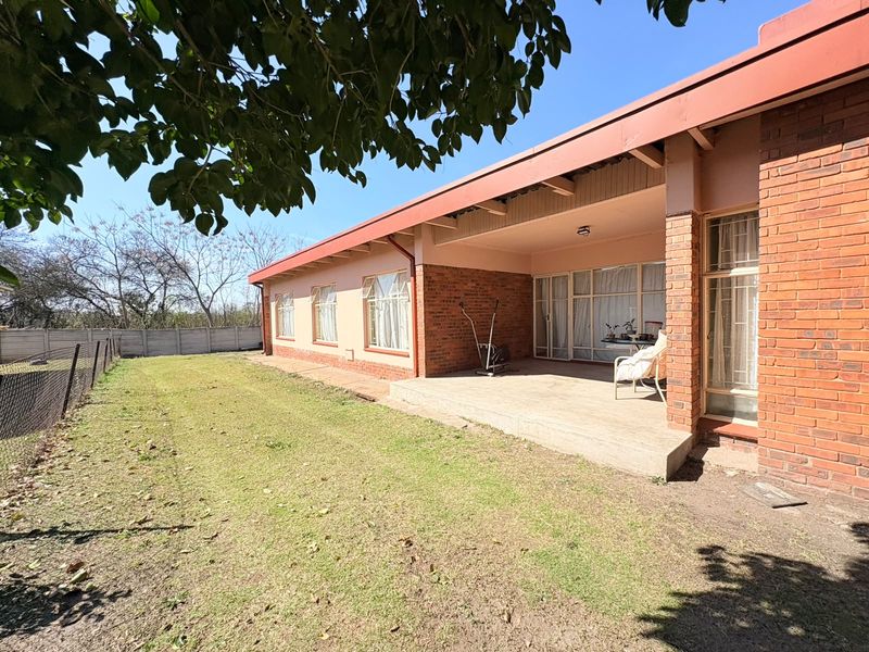 Rear view of the house featuring a brick facade, a covered concrete patio, and a spacious backyard enclosed by a precast boundary wall.