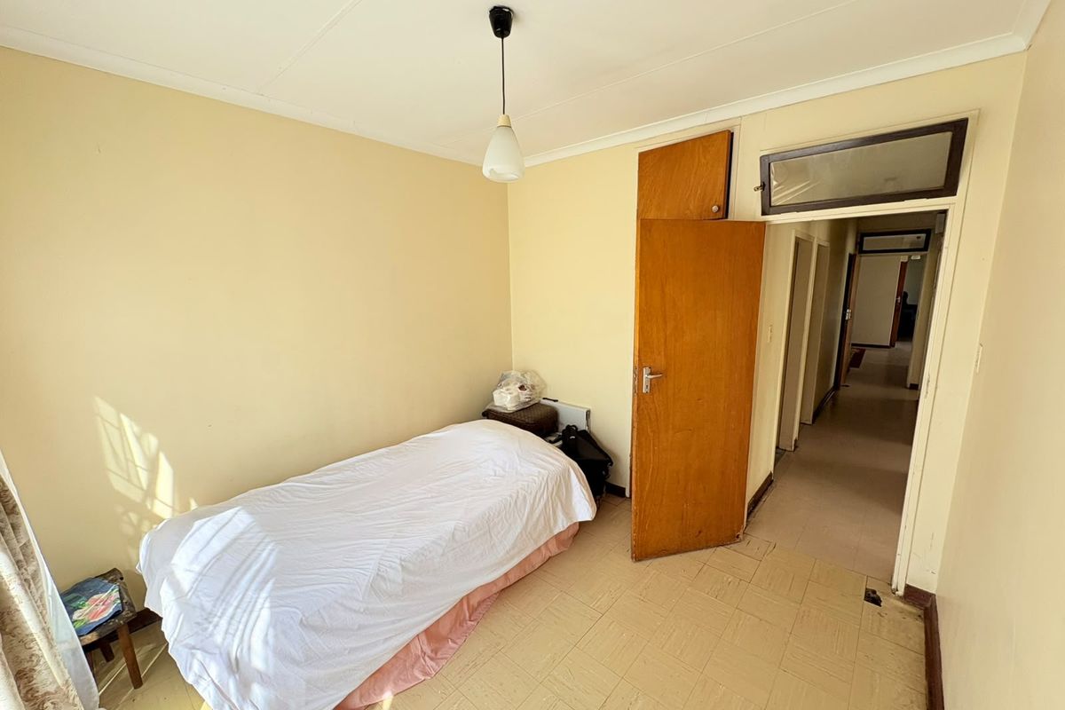 A simple bedroom featuring tiled flooring, a built-in cupboard, and a pendant light fixture, offering a functional space ready for cosmetic updates.