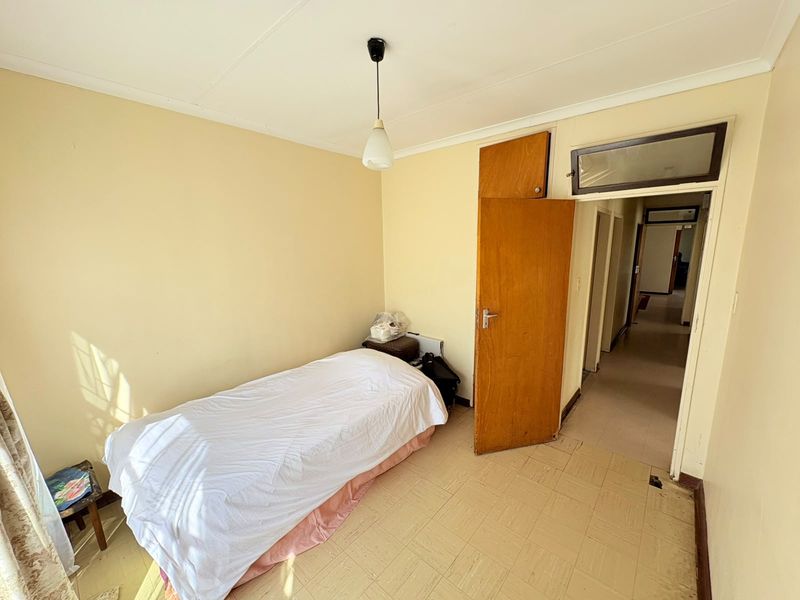 A simple bedroom featuring tiled flooring, a built-in cupboard, and a pendant light fixture, offering a functional space ready for cosmetic updates.