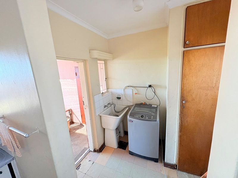 A functional laundry area featuring a utility sink, built-in storage cabinetry, and tiled flooring with direct access to an outdoor space.