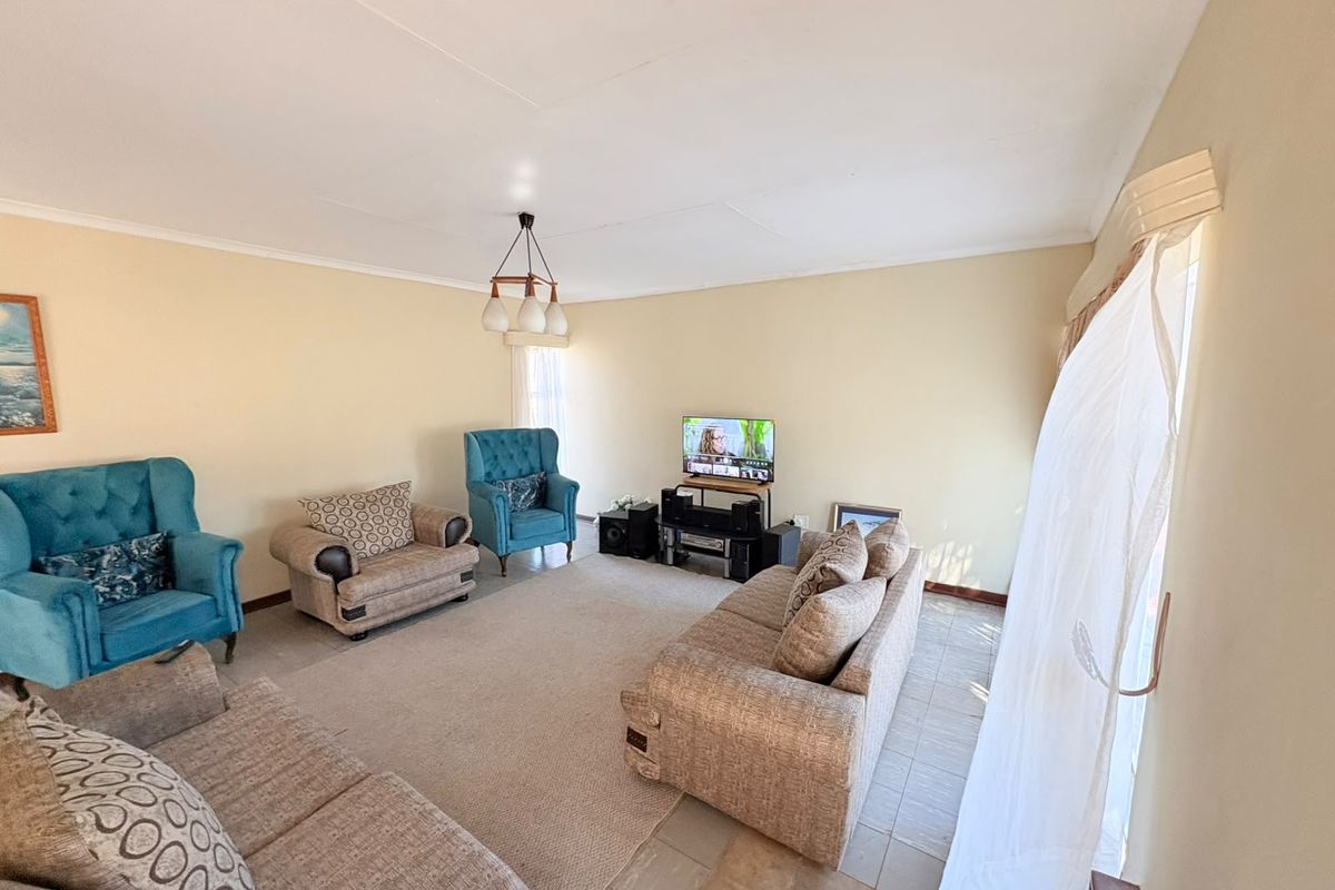 A spacious living room featuring neutral wall tones, tiled flooring, and natural light through large windows.