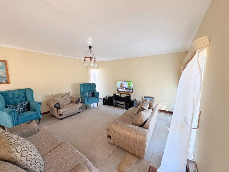 A spacious living room featuring neutral wall tones, tiled flooring, and natural light through large windows.