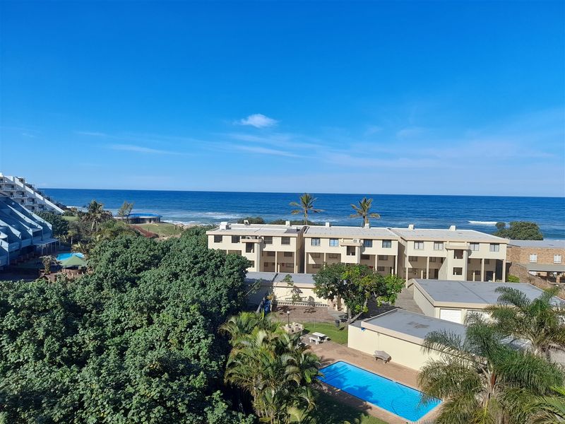 Elevated coastal view overlooking the apartment complex, swimming pool, and lush surrounding gardens with direct ocean vistas.