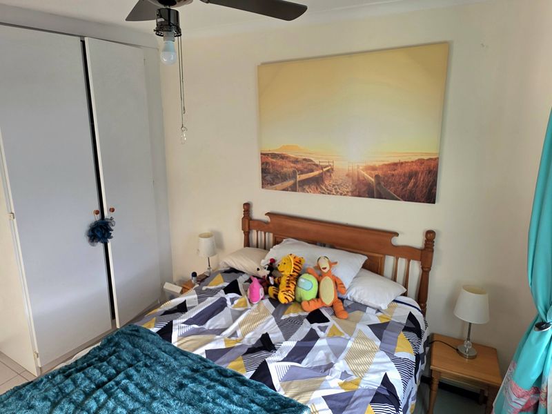 A functional bedroom featuring a built-in wardrobe, ceiling fan, and tiled flooring, with security bars installed on the window for added safety.