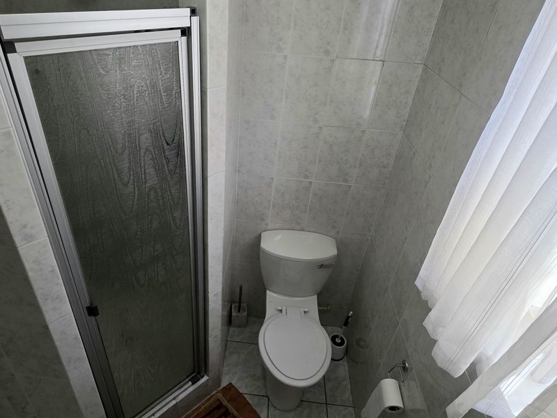 A compact bathroom featuring a shower enclosure, toilet, and neutral wall and floor tiling.