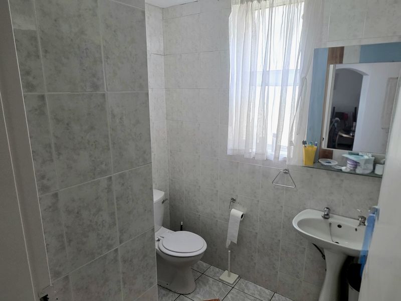 A functional bathroom featuring tiled walls and flooring, a pedestal sink, and a standard toilet, providing a clean and practical space.