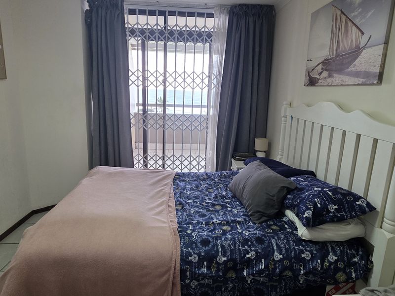A bedroom featuring tiled flooring and a sliding glass door with a security gate, providing access to an outdoor balcony area.