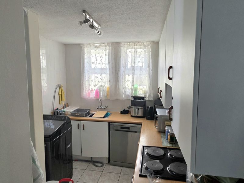 A compact kitchen featuring built-in cabinetry, laminate countertops, a stainless steel sink, and an electric hob, with tiled flooring throughout.