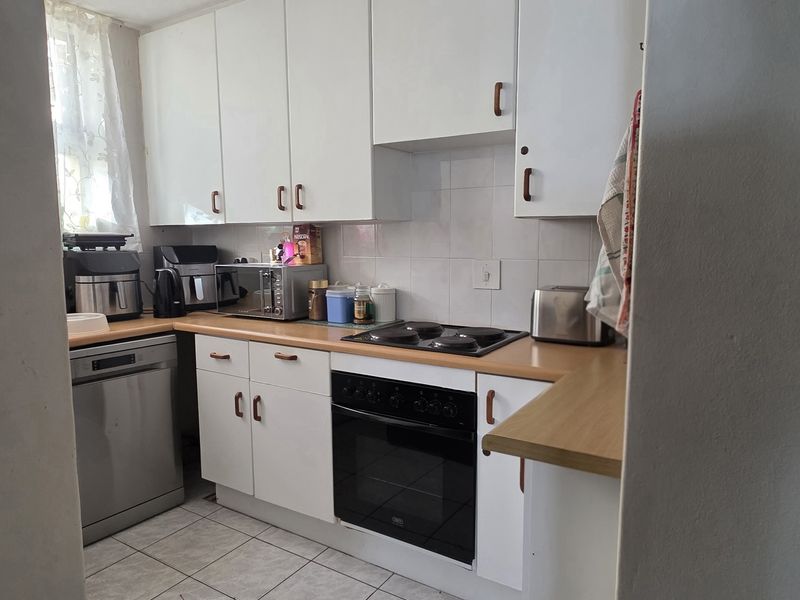 A functional kitchen featuring white cabinetry, laminate countertops, a built-in oven with electric hob, and tiled flooring.