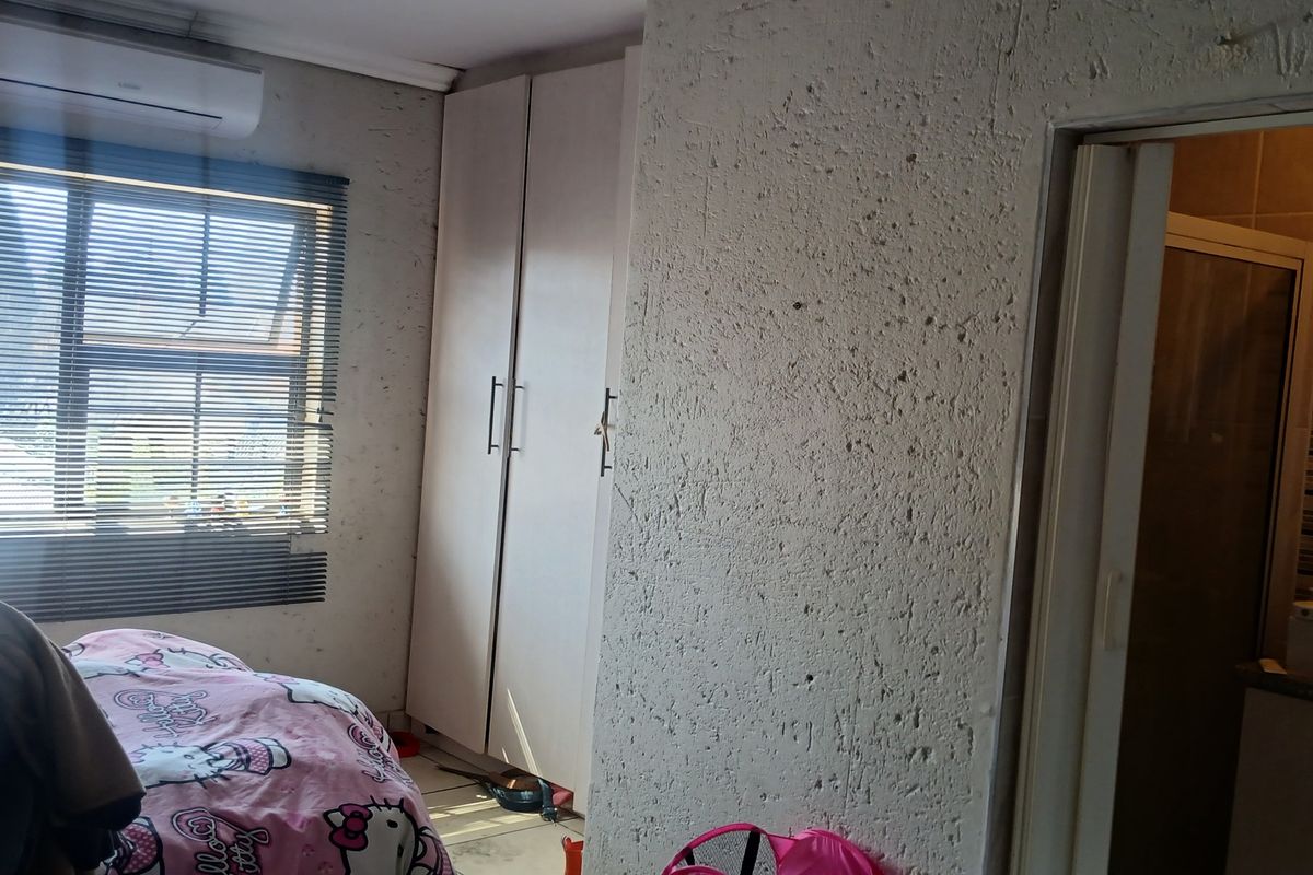 Bedroom featuring built-in cupboards, an air conditioning unit, and textured wall finishes, with an adjoining en-suite bathroom.