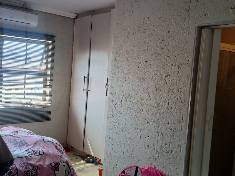 Bedroom featuring built-in cupboards, an air conditioning unit, and textured wall finishes, with an adjoining en-suite bathroom.