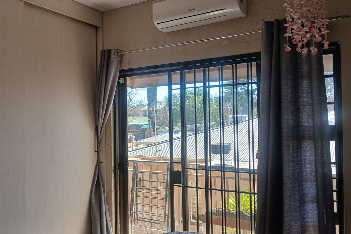 A bedroom featuring a built-in cupboard, split-system air conditioner, and a sliding glass door with security gate leading to an outdoor area.
