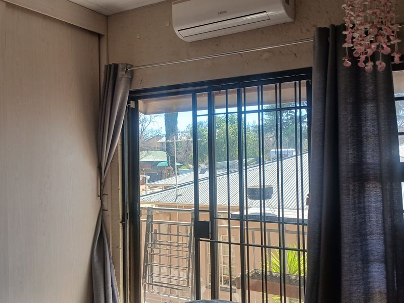 A bedroom featuring a built-in cupboard, split-system air conditioner, and a sliding glass door with security gate leading to an outdoor area.