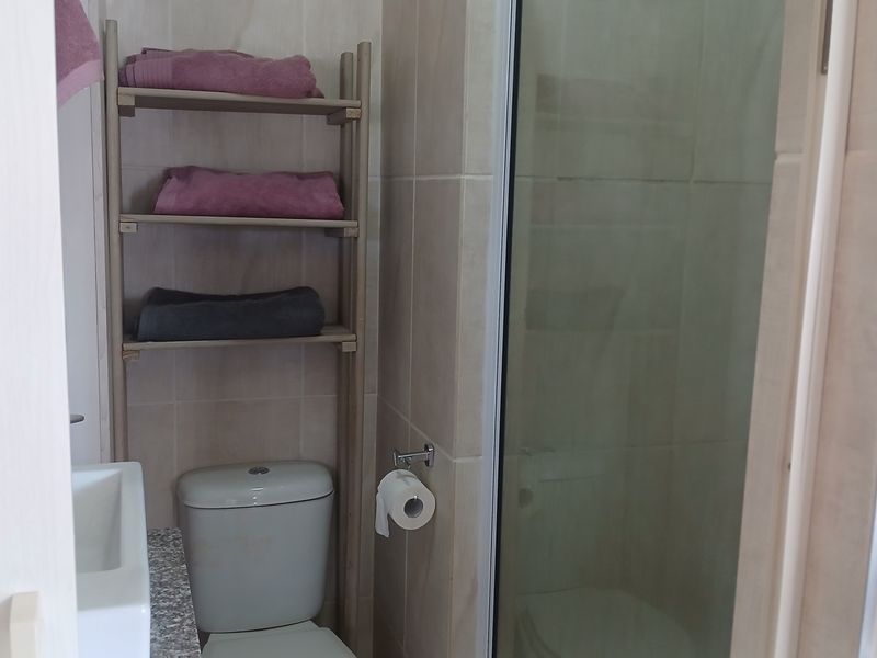 A functional bathroom featuring a shower enclosure, toilet, and vanity with a granite countertop, finished with neutral wall tiles.