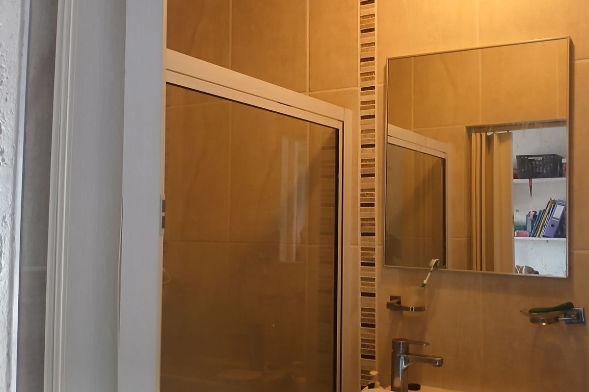A functional bathroom featuring a shower enclosure, tiled walls with decorative accents, a wall-mounted mirror, and a modern basin mixer tap.