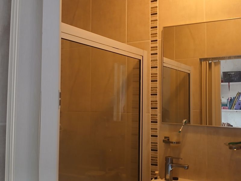 A functional bathroom featuring a shower enclosure, tiled walls with decorative accents, a wall-mounted mirror, and a modern basin mixer tap.