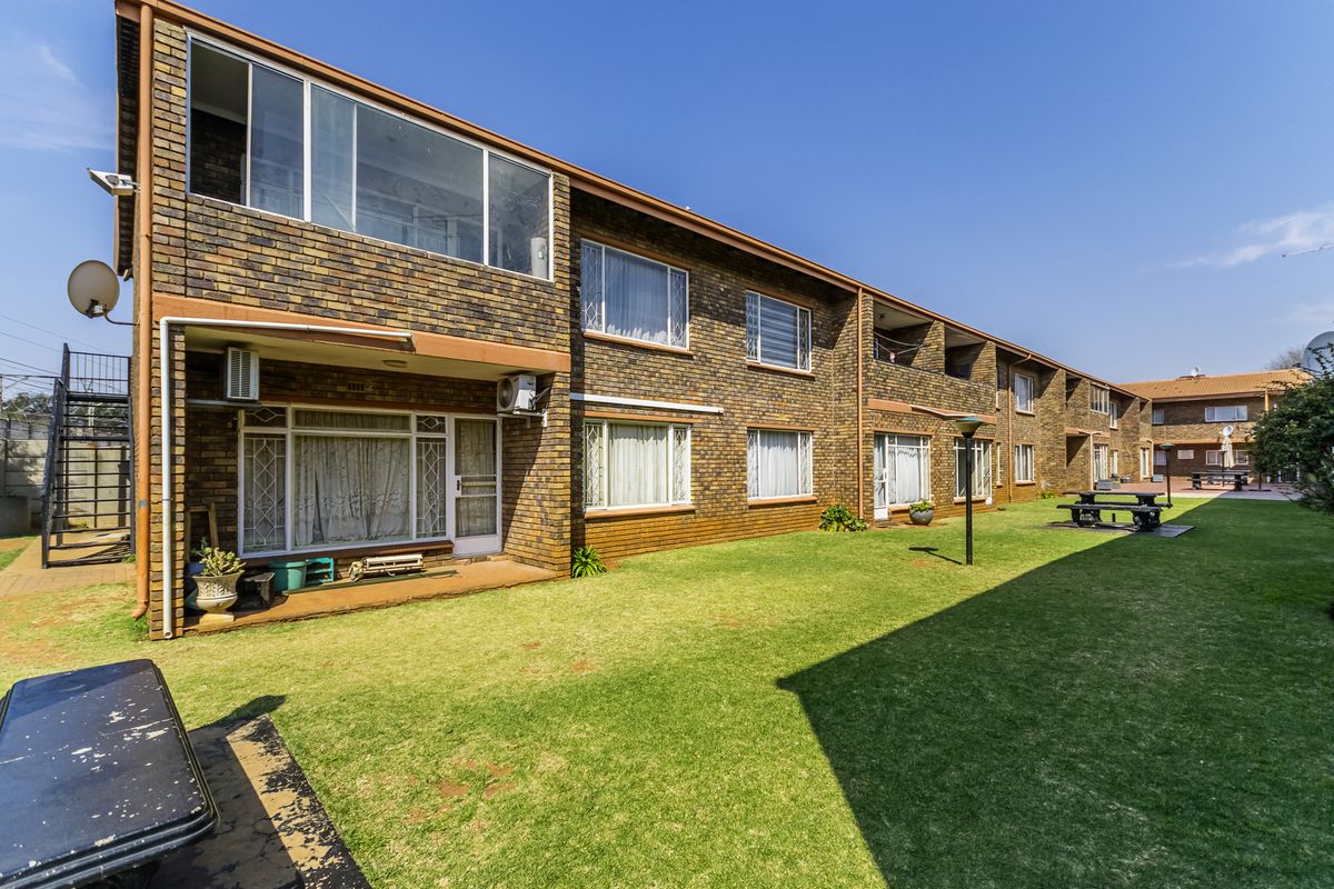 Rear view of a multi-story apartment complex featuring face brick construction, ground floor patio access, and a shared communal garden space.