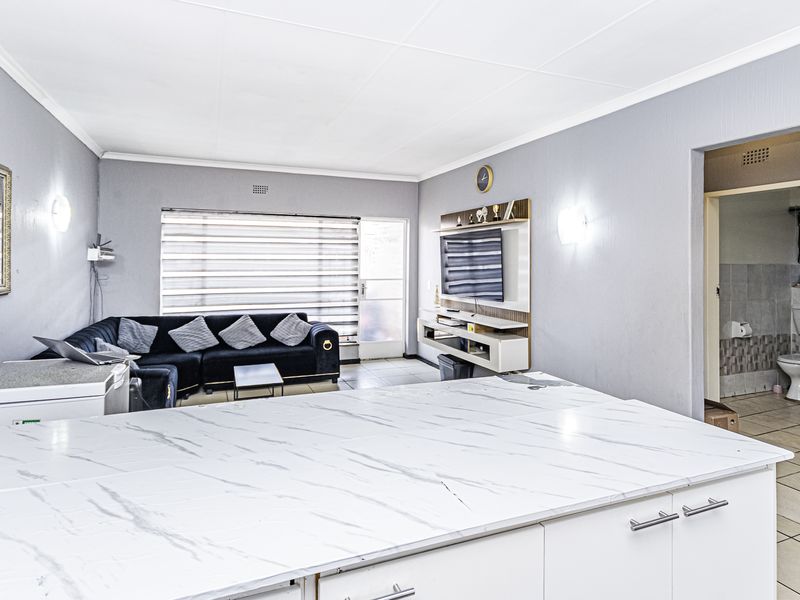 Open-plan living area featuring a modern kitchen island with marble-look countertop, tiled flooring, and a built-in media unit, with an adjacent bathroom entrance.