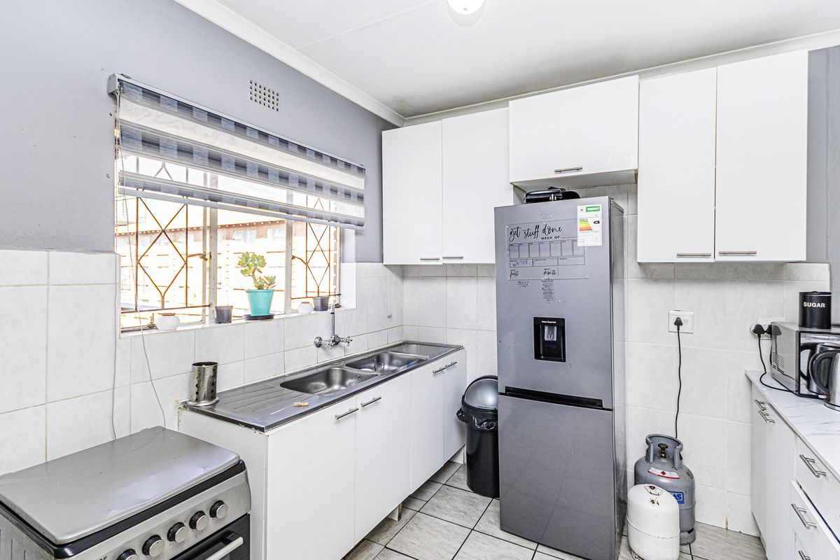 Functional kitchen featuring white cabinetry, double bowl stainless steel sink, tiled splashbacks, and tiled flooring with security bars on the window.