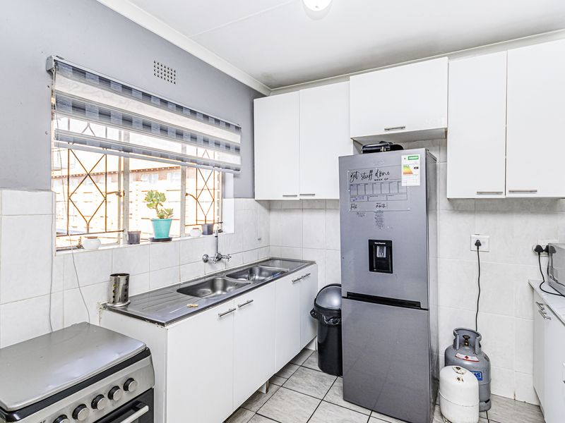 Functional kitchen featuring white cabinetry, double bowl stainless steel sink, tiled splashbacks, and tiled flooring with security bars on the window.