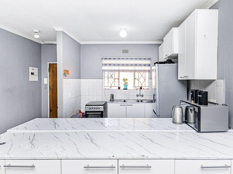 A functional kitchen featuring white cabinetry, marble-effect countertops, a tiled backsplash, and a built-in stove, offering a clean and practical workspace.