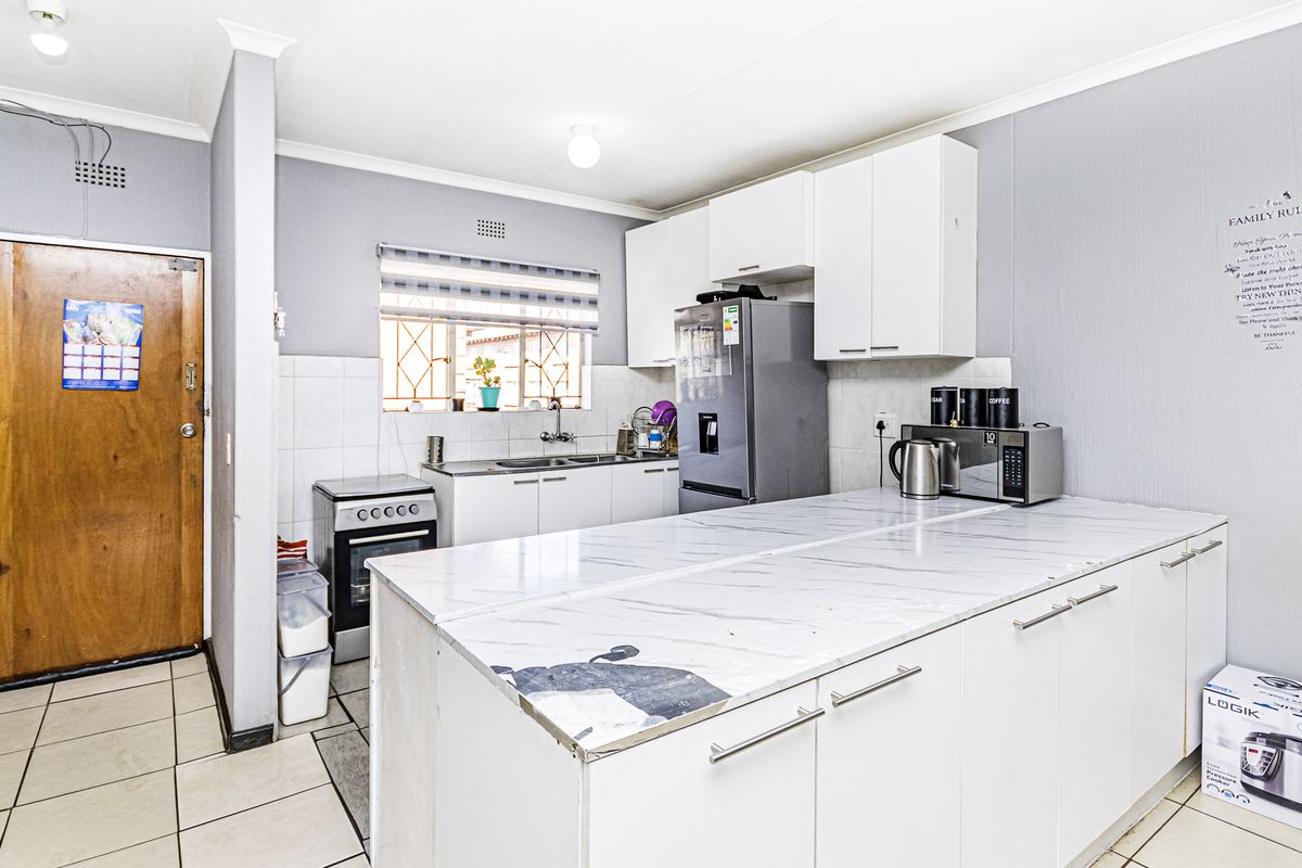 Functional kitchen featuring white cabinetry, marble-look countertops, tiled backsplash, and a freestanding stove, offering a practical layout for daily meal preparation.