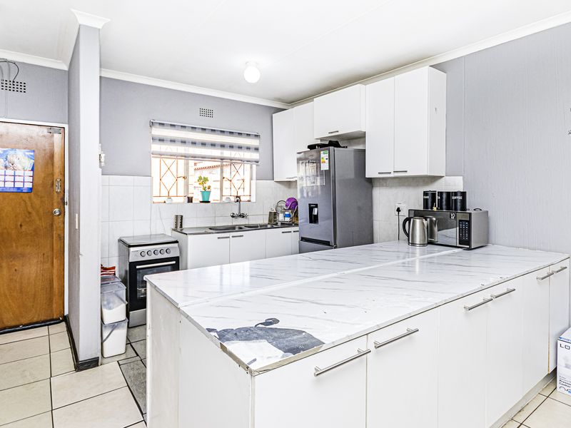 Functional kitchen featuring white cabinetry, marble-look countertops, tiled backsplash, and a freestanding stove, offering a practical layout for daily meal preparation.